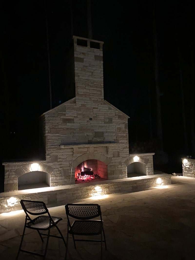Lit stone outdoor fireplace with built-in wood storage