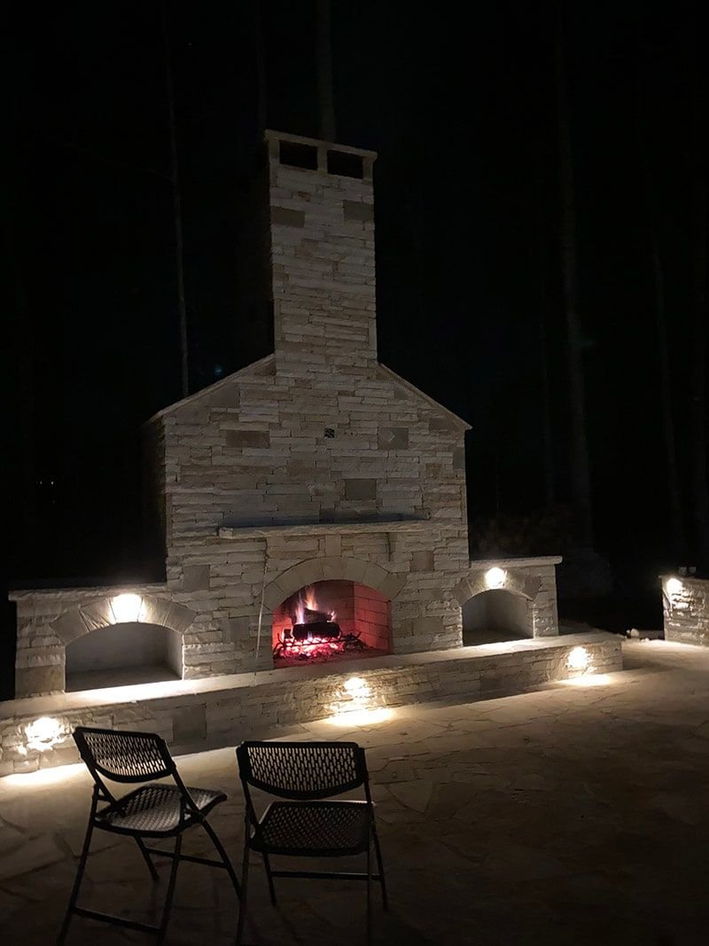 Lit stone outdoor fireplace with built-in wood storage