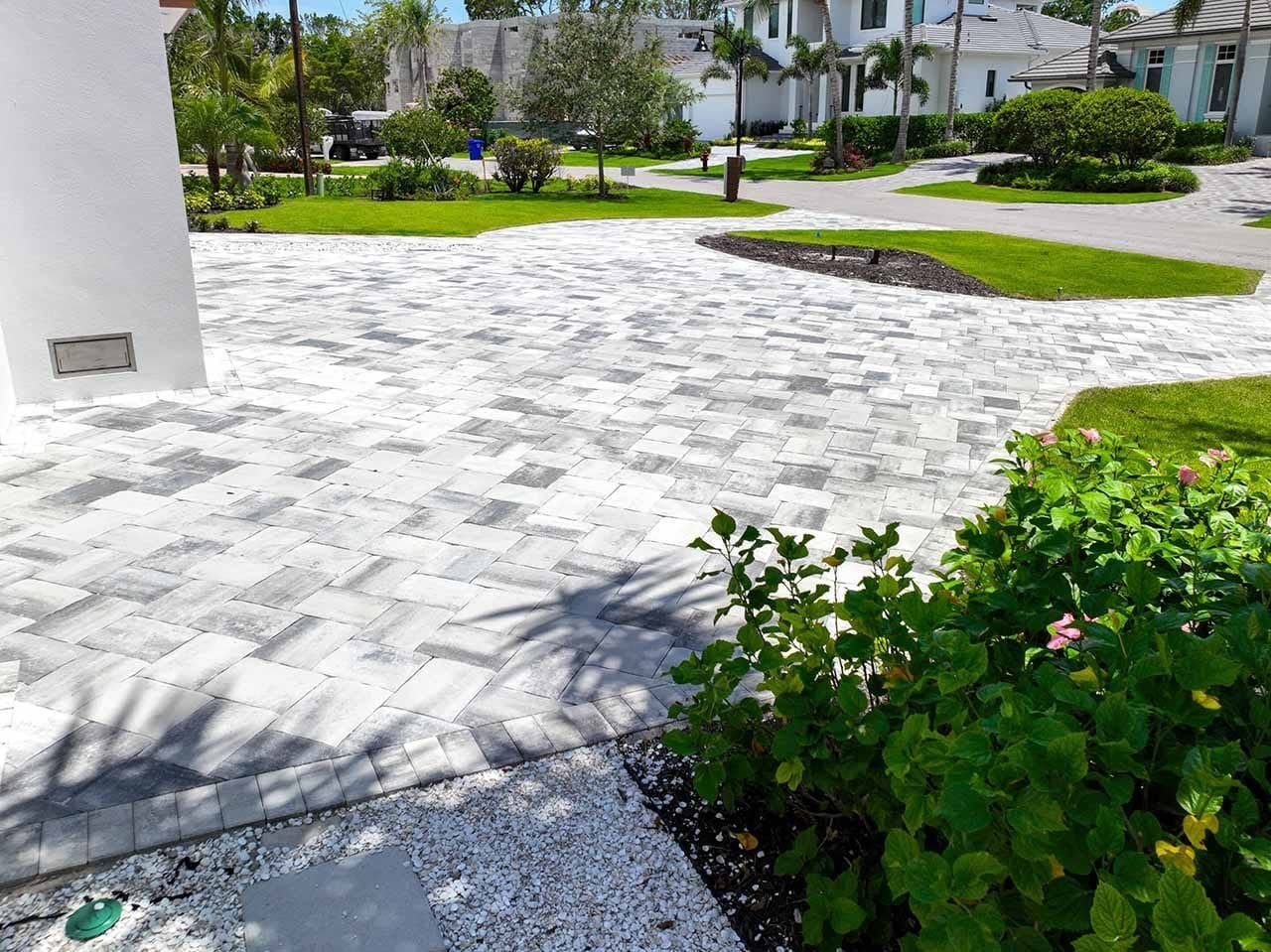 Light travertine-look paver driveway with landscaped borders